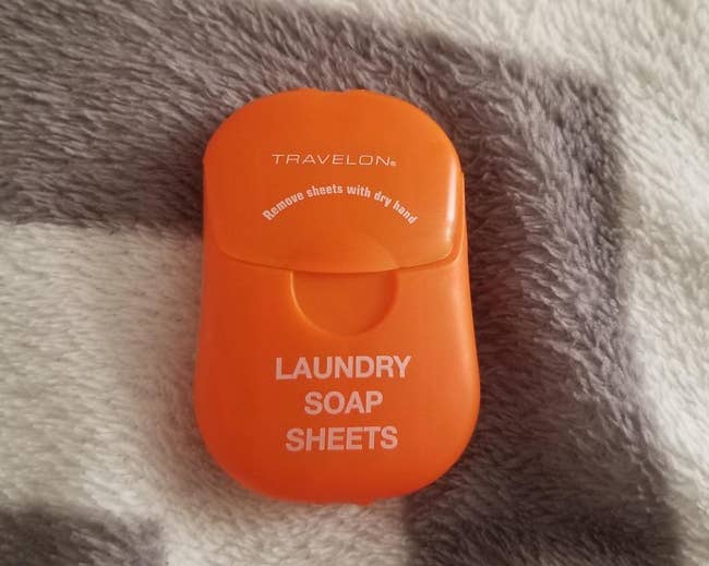 reviewer's orange pack of laundry soap sheets on top of a blanket