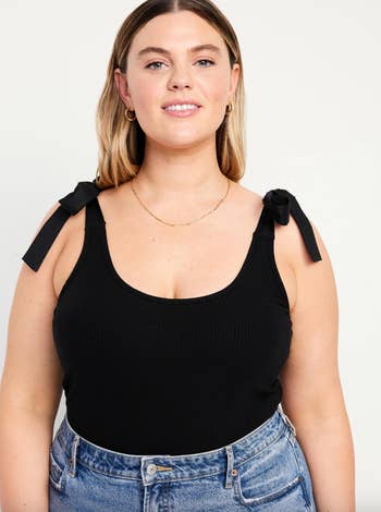 Model in a black sleeveless top with bow details on shoulders