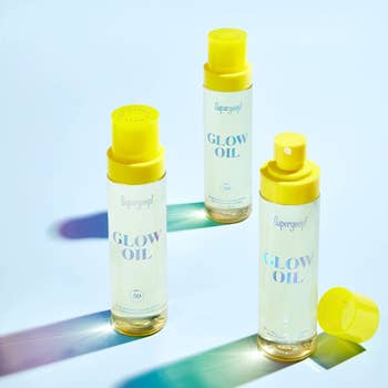 three bottles of glow oil with yellow tops on a light blue background