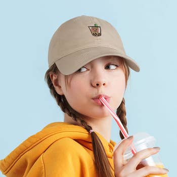 Model in khaki baseball cap with embroidered boba tea smiling on the front 