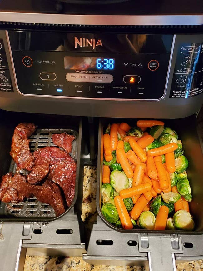 a reviewer photo of the two baskets from the air fryer one with cooked meat on one side and cooked veggies on the other side