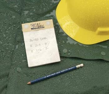 Notepad with calculations next to a pencil on a wet surface, implying outdoor work or planning