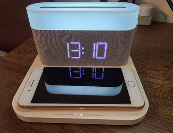 A white and gray L-shaped clock with a digital numeral display and a flat surface to charge a phone 