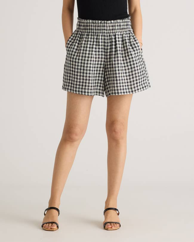Person wearing gingham shorts with hands in pockets, styled with a sleeveless top and sandals
