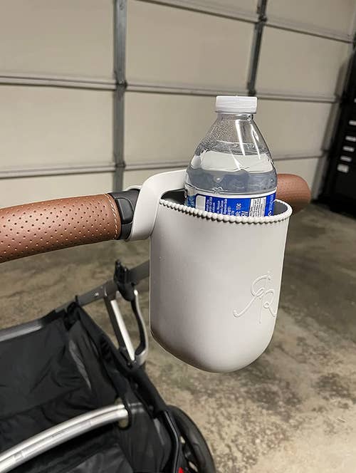 A white silicone cup holder wrapped around a stroller handle holding a water bottle 