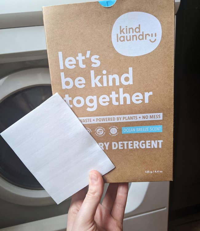 a hand holding a box of laundry sheets and a single sheet of detergent 