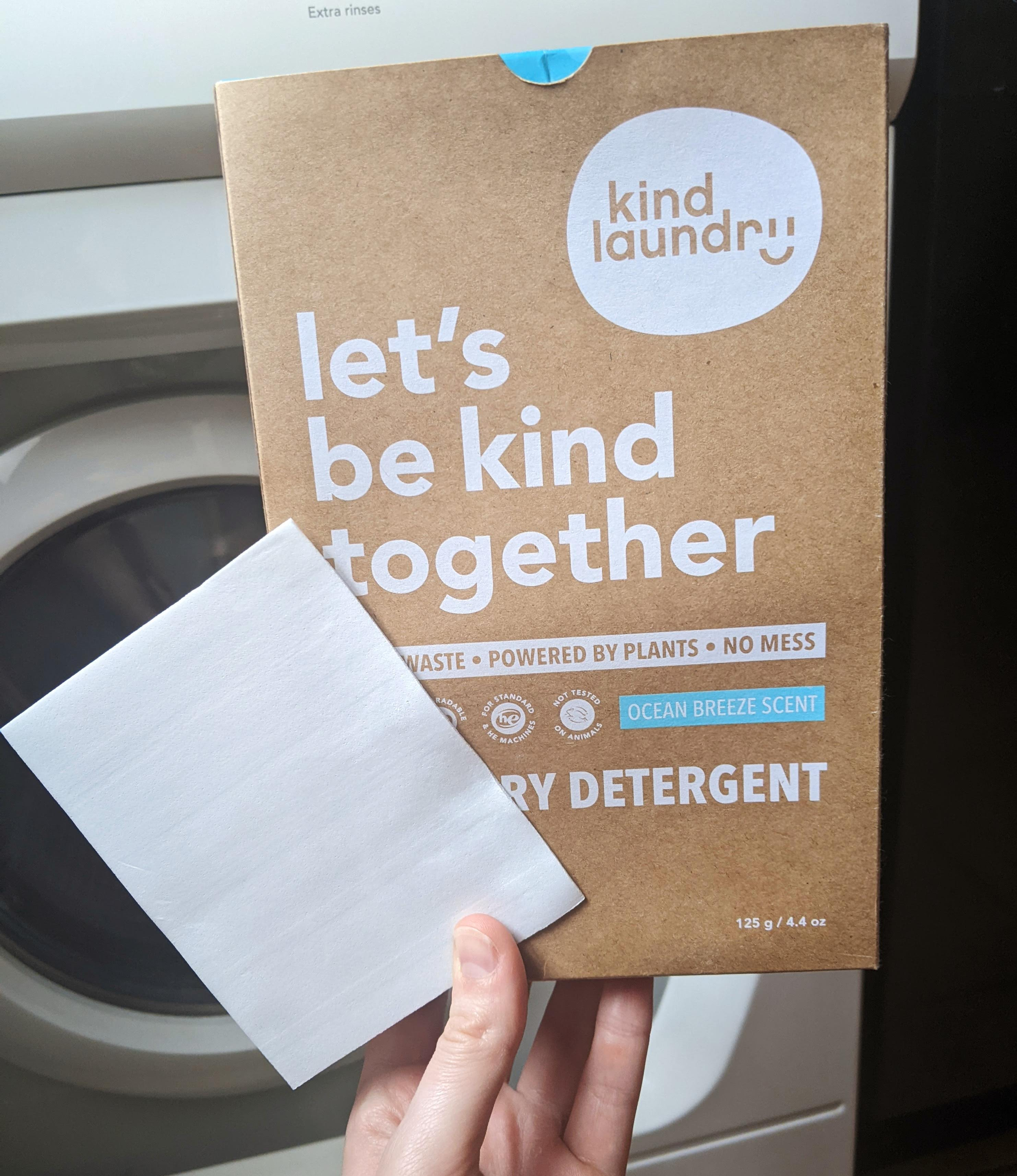 a hand holding a box of laundry sheets and a single sheet of detergent