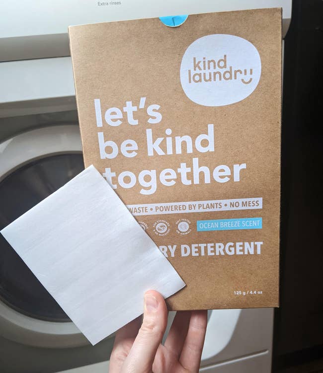 a hand holding a box of laundry sheets and a single sheet of detergent 