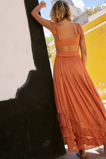 Person in a flowing maxi dress with ruffled straps and hem, standing outdoors against a wall, showcasing a relaxed, bohemian style