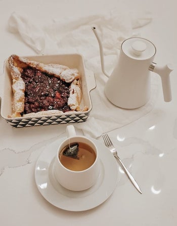 reviewer's white kettle on a table with a cup of tea and a dessert