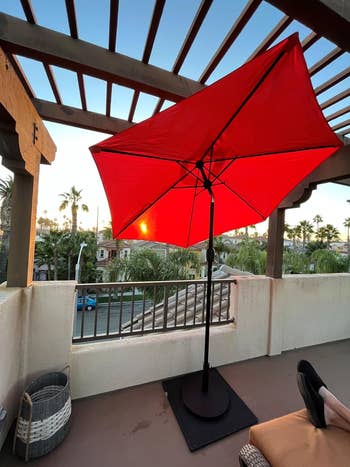Balcony with a ample  reddish  umbrella, a basket, and a person's legs disposable   connected  a relaxing seat