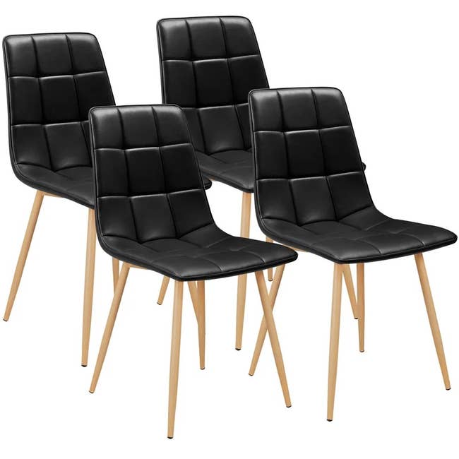 A set of four black faux leather woven chairs with brown legs