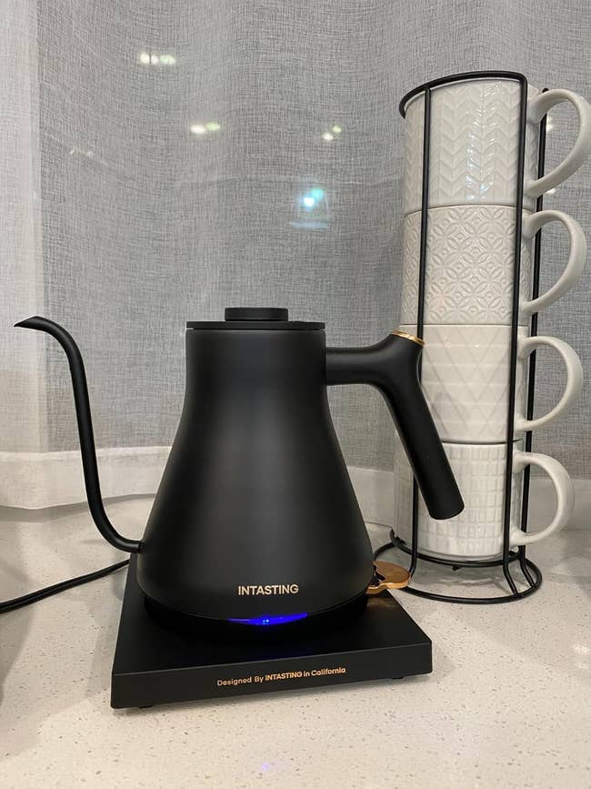Electric kettle with a sleek plan  adjacent  to a stack of patterned mugs connected  a countertop