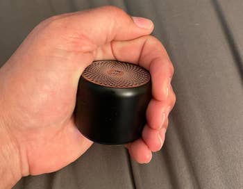 Person holding a small, portable speaker in their hand