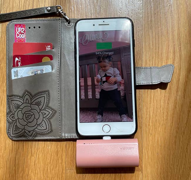 A smartphone placed in a wallet case with a portable charger charged into the phone