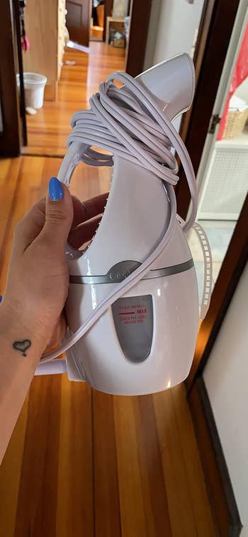 A hand holding a Conair steamer with a coiled cord, indoors