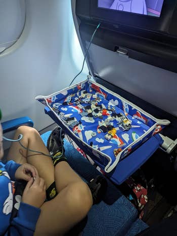 reviewer sitting on a plane with the airplane patterned tray cover on the tray