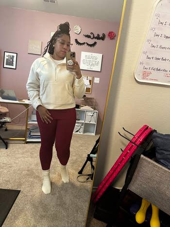 Person in a white hoodie and red leggings taking a mirror selfie in a room with exercise equipment