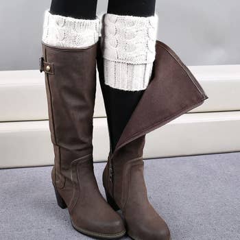 model wearing the white boot cuffs under a pair of tall dark brown boots, with one boot unzipped to show the full boot cuff underneath