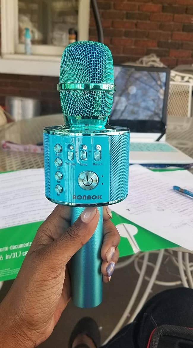 Person holding turquoise karaoke microphone outdoors, with papers and a laptop successful the inheritance connected a patio table