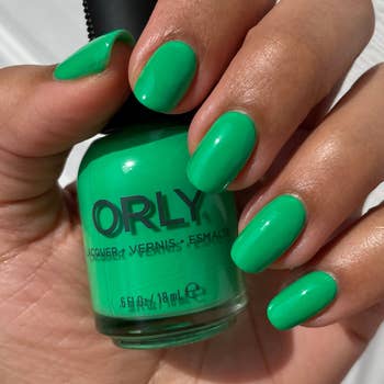 model holding a bottle of the kelly green polish and wearing it on their nails