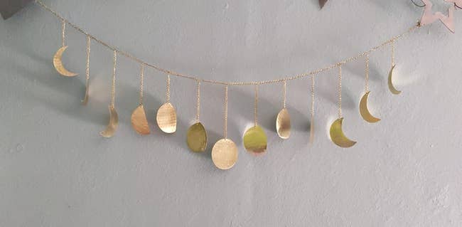 a reviewer photo of metallic garland with moon pendants hanging from it 