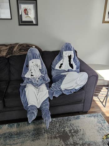 Two people dressed in shark onesies sit on a couch