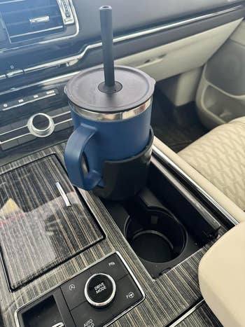 Mug perjalanan berwarna biru dengan penutup dan sedotan ditempatkan di tempat cangkir mobil