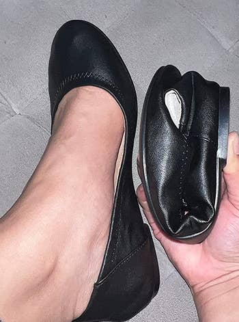 reviewer wearing one of the black flats and holding the other, which is folded in half