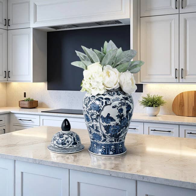 Decorative blue and white vase with white flowers and green leaves, set on a kitchen island with elegant cabinetry in the background