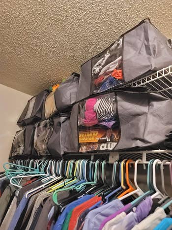 another reviewer's four grey storage containers full of clothes stored on top of closet shelves