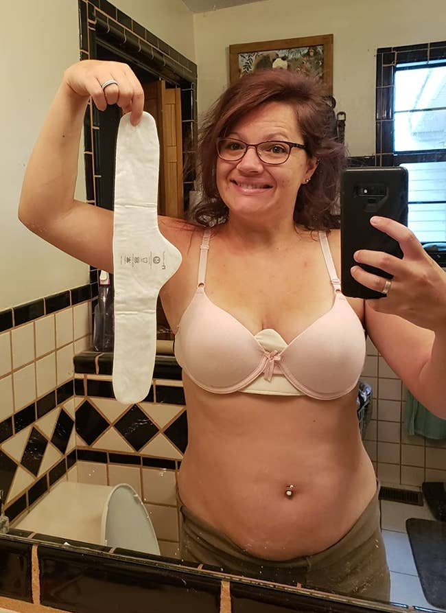 a reviewer smiling while wearing a bra with one of the liners and holding another liner 