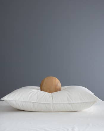 A round wooden object rests on a plush white pillow