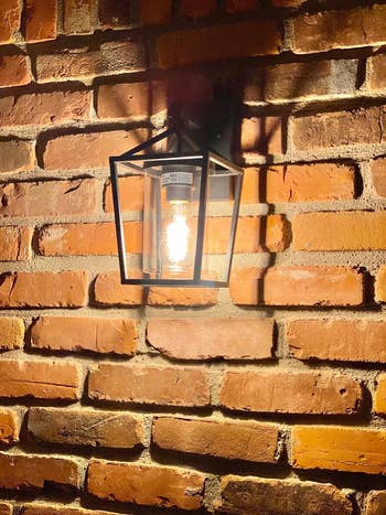 reviewer's wall-mounted outdoor lantern with a visible filament bulb, affixed to a brick wall, providing ambient lighting