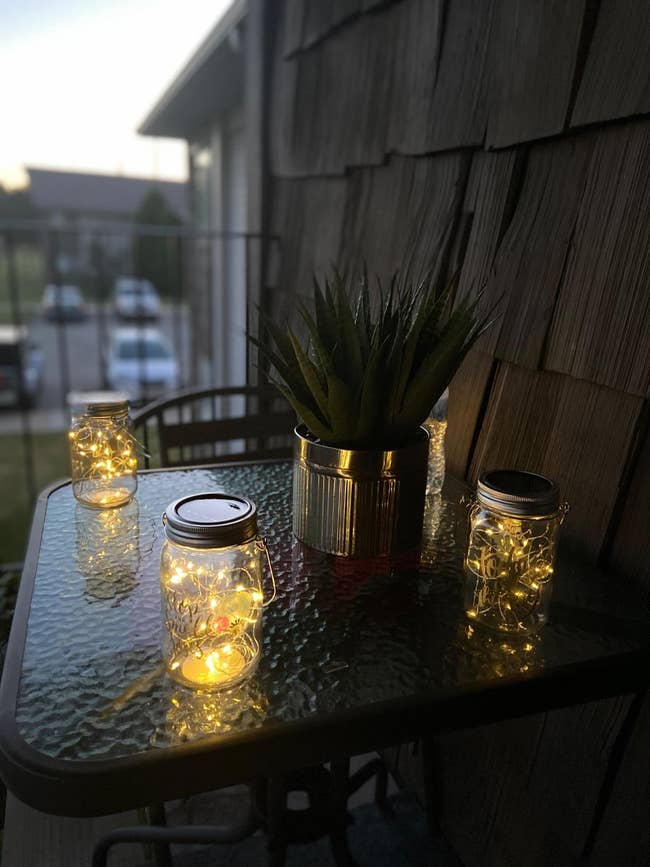 Decorative glass jars with string lights inside on an outdoor table at dusk, providing ambient lighting
