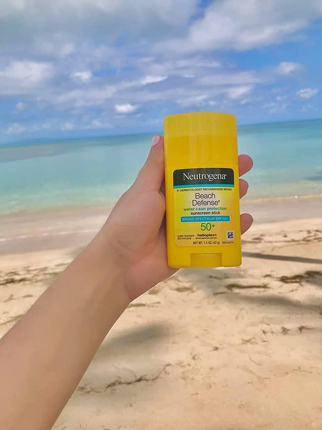 image of reviewer holding up the sunscreen stick while on a beach