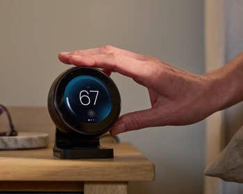 A manus  adjusts a astute  thermostat connected  a woody  surface, acceptable   to 67 degrees