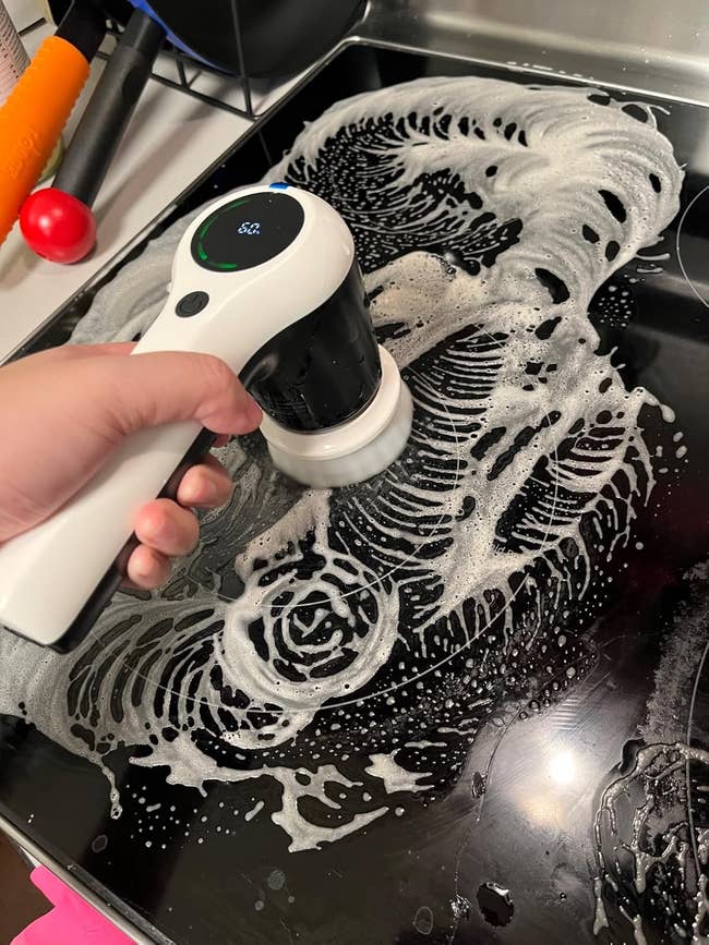 A manus uses an electrical scrub brushwood to cleanable a stovetop with soapy suds