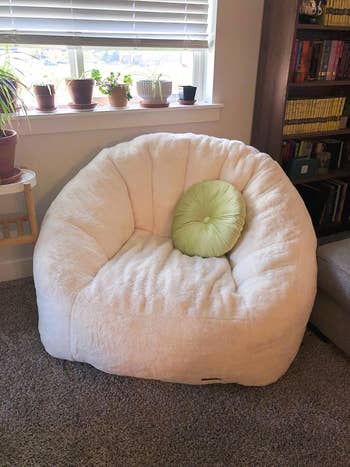 another reviewer's plush achromatic  legume  container  seat  with a greenish  circular  pillow, placed successful  a cozy country   adjacent   a bookshelf and model   with potted plants