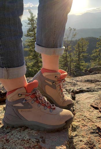 Person wearing hiking boots standing on a rocky overlook with a scenic mountain view