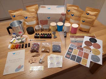 Candle-making kit with various waxes, essential oils, wicks, containers, and design labels displayed on a wooden table