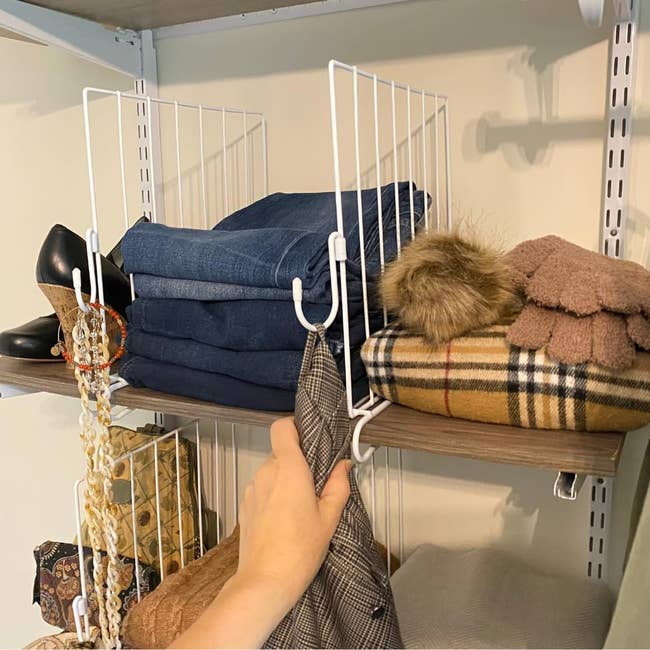 person hanging plaid garment connected support with folded jeans, hat, scarf, and shoes that are separated by support dividers with hanging jooks ont hem