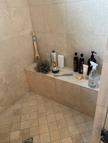 reviewer's shower with built in bench covered with toiletry bottles