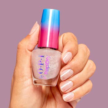 Hand holding OPI nail polish with a gradient cap, showcasing sparkly pastel nails against a plain background. Suitable for shopping content