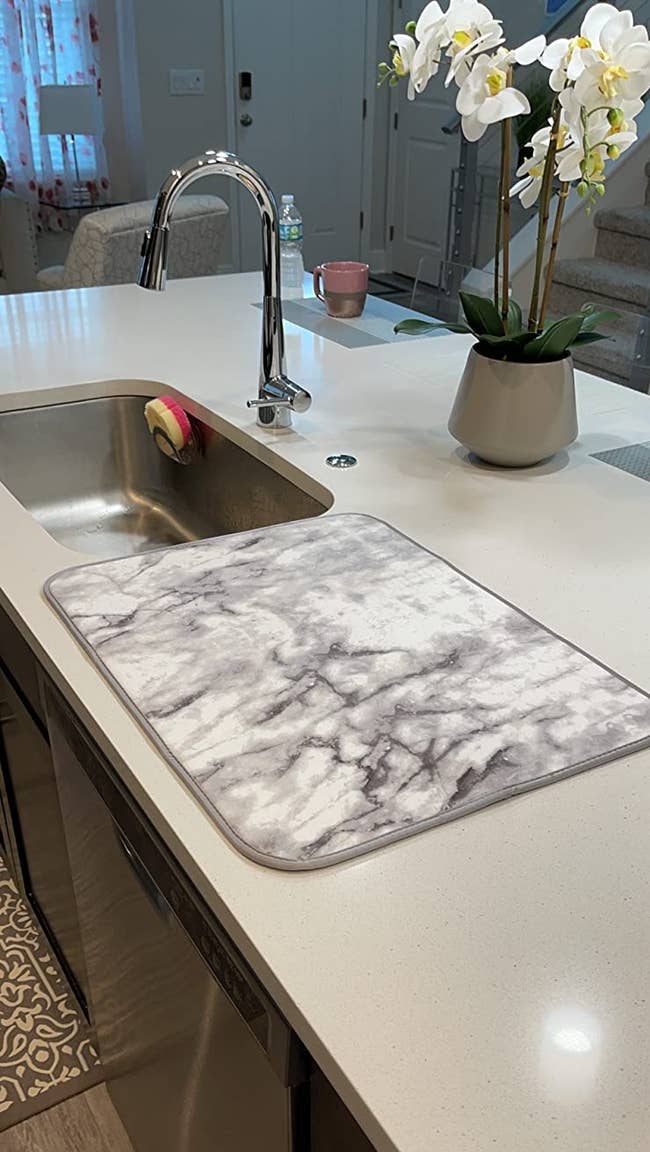 reviewer image of the marble-patterned dish drying mat on a kitchen counter next to a sink
