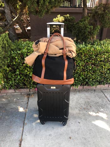 reviewer's black weekender bag on top of a rolling suitcase