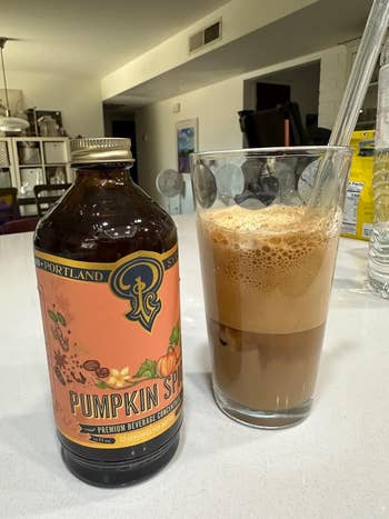 A vessel  of pumpkin spice beverage ore  adjacent  to a solid  of iced pumpkin spice latte connected  a room  counter