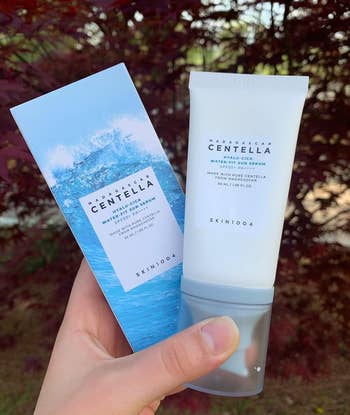 Hand holds a Centella skincare product against a natural backdrop