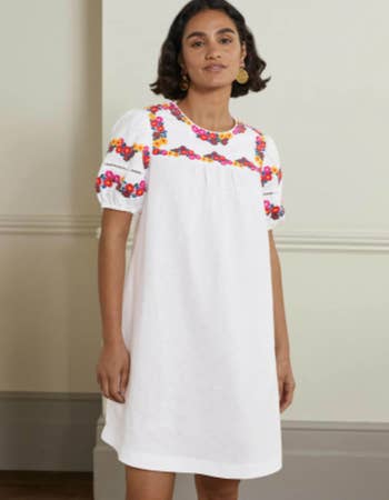 model in white short sleeve mini with colorful flowers at sleeves and yoke
