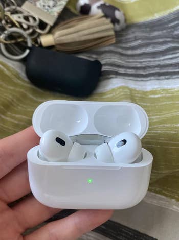 reviewer holding the airpods in their charging case with the green charging light on